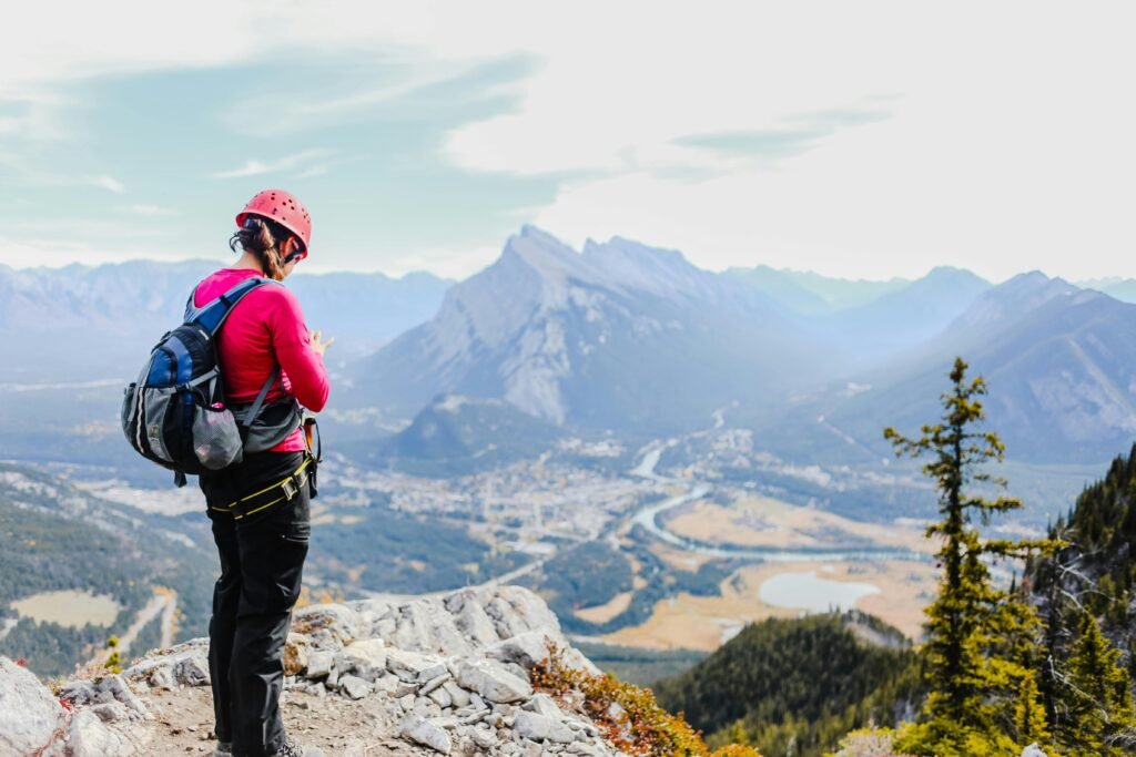 Woman wearing a pink sweater and helmet hiking on a mountain cliff with a scenic view.